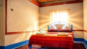 Une pièce avec un lit, une fenêtre avec des rideaux, un tapis à motifs et un interrupteur mural.
