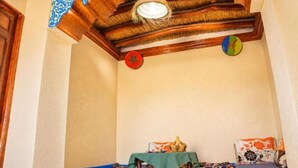 Een kamer met een houten plafond, een hanglamp, een wandklok en een tafeltje met een mandje.