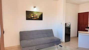 Una sala de estar con un sofá gris, una mesa de centro de vidrio y un cuadro en la pared.