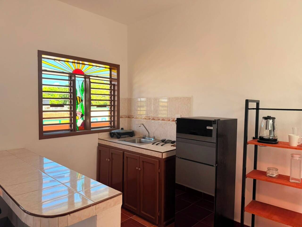 A compact kitchen with a built-in refrigerator, a sink, and a window with a stained glass design.