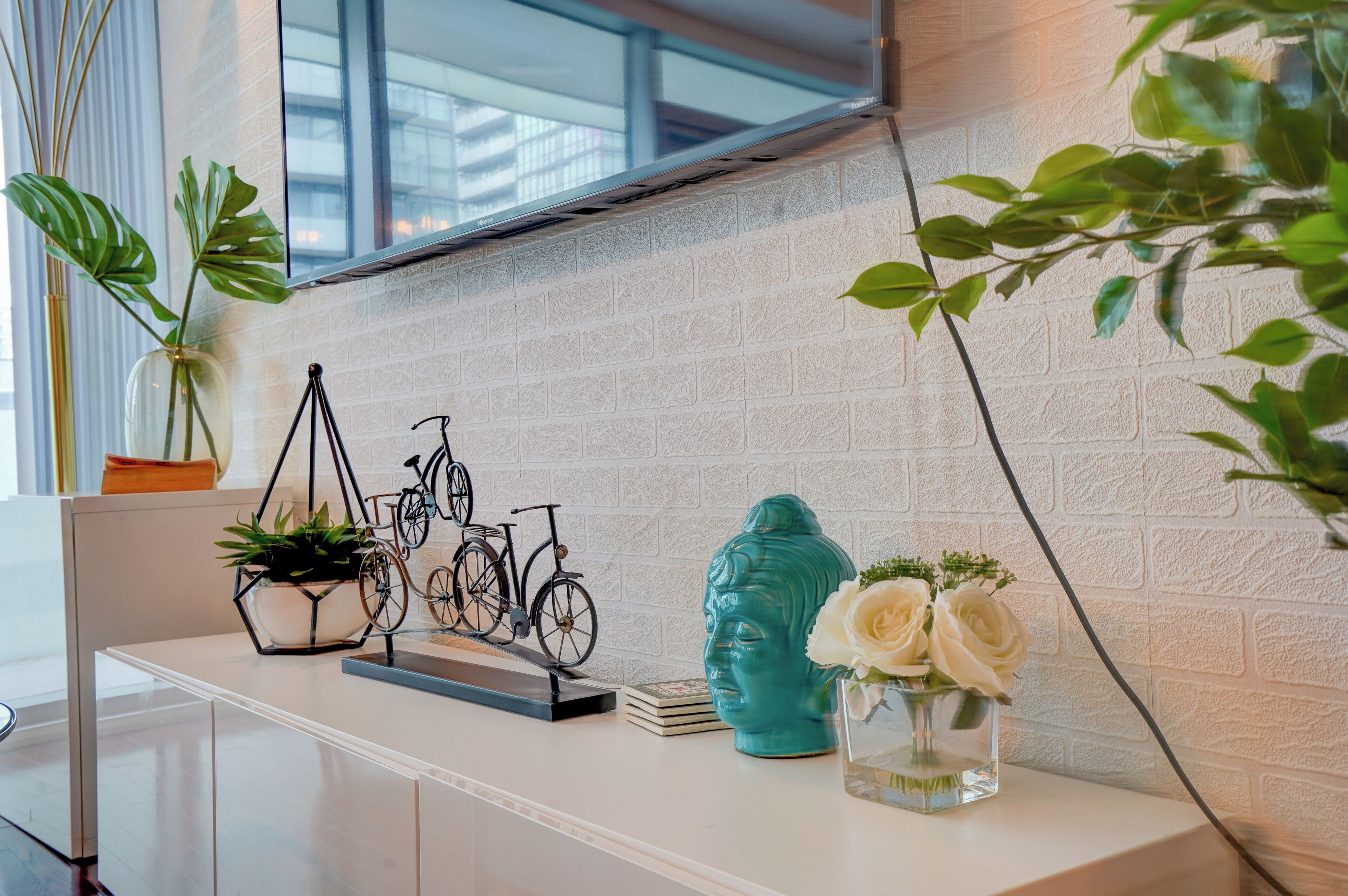 A white console table with a potted plant, a decorative metal sculpture, a ceramic bust, and a vase with white flowers.