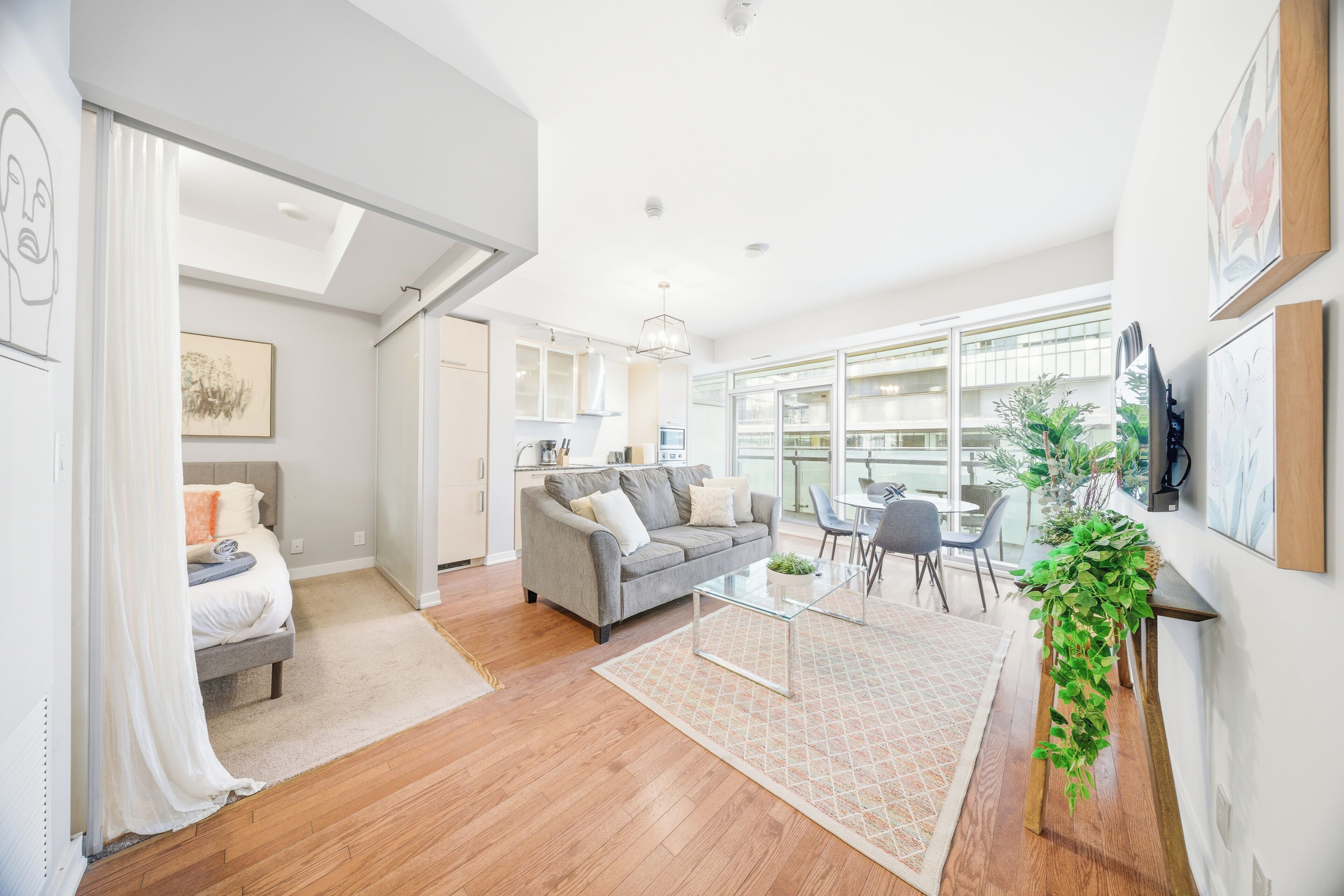 A modern living room with a grey sofa, a glass coffee table, and a dining area with chairs.