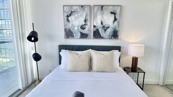 A hotel room with a large bed, two side tables, a window with curtains, and abstract artwork on the wall.