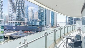 A balcony with a glass railing overlooking a cityscape with modern buildings. - Wanderlust Suites (Toronto)