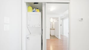A laundry room with a white washing machine and detergent bottles. - Wanderlust Suites (Toronto)