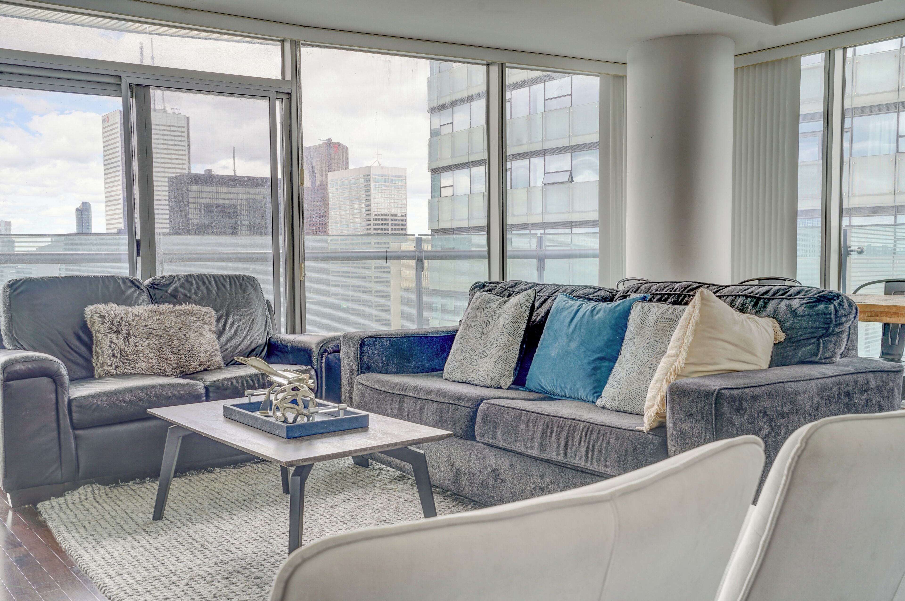 A modern living room with a grey sofa set, a coffee table, and a view of the cityscape through large windows.