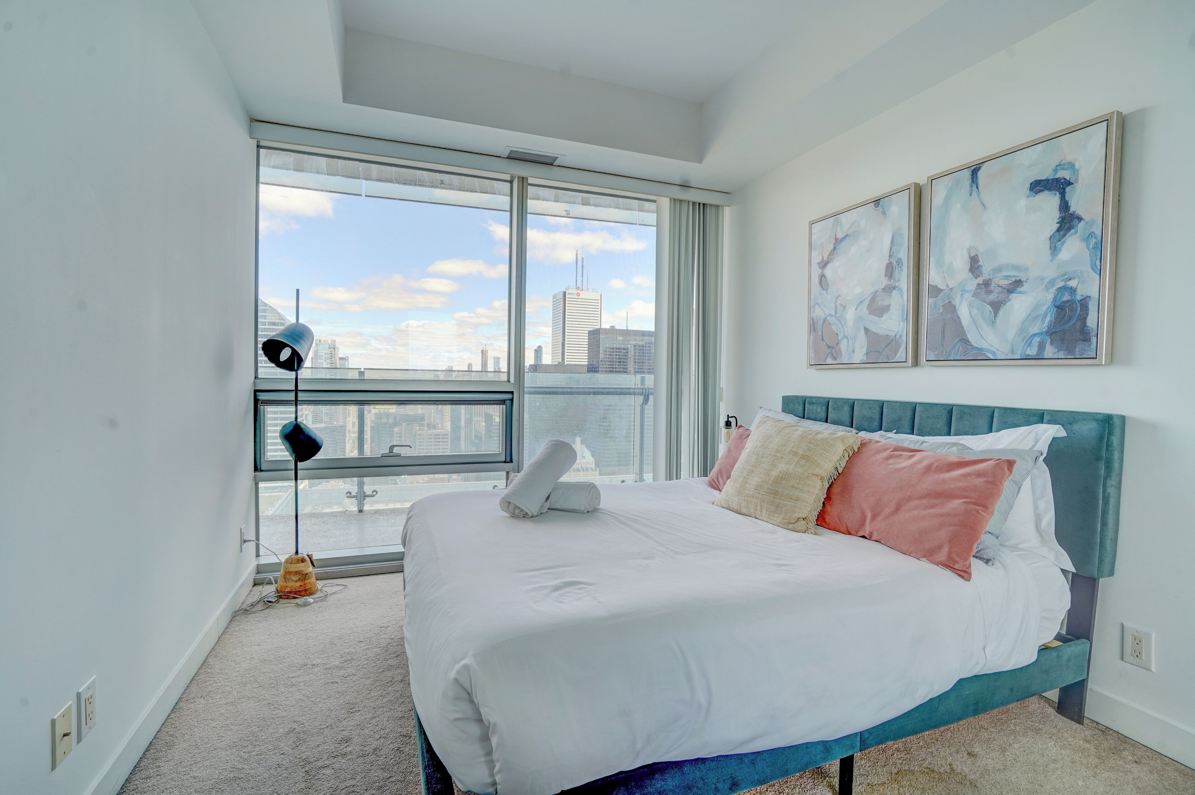 A modern bedroom with a large bed, city view, and abstract art.