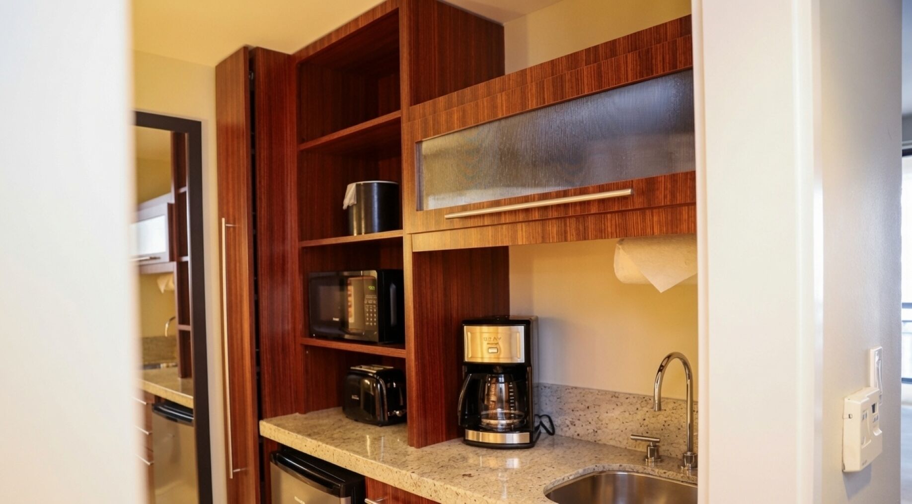 A compact kitchen with wooden cabinets, a coffee maker, and a stainless steel sink.