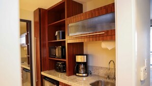 A compact kitchen with wooden cabinets, a coffee maker, and a stainless steel sink.