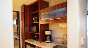 Una cocina compacta con armarios de madera, una cafetera y un lavamanos de acero inoxidable.