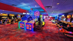 An indoor arcade with various gaming machines, a patterned carpet, and a ceiling with a grid pattern.