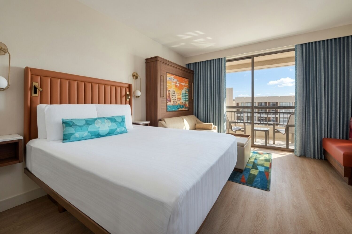 A hotel room with a large bed, a desk, a chair, a view of the city, and a balcony.