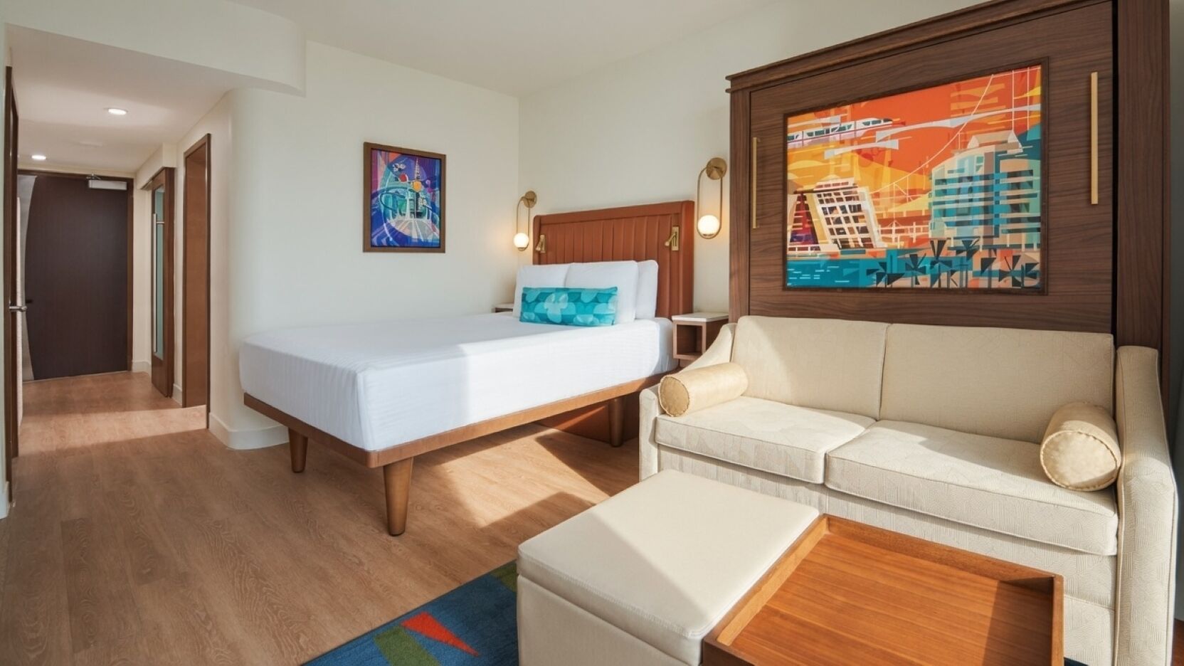 Quarto de hotel com cama, sofá, mesa de centro, quadro e TV na parede.