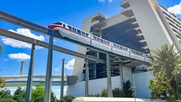 Een modern gebouw met een overdekt terras en een trein op een verhoogd spoor.