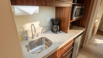 Una cucina compatta con lavandino in acciaio inossidabile, mobili in legno, macchina da caffè e microonde.