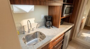 A compact kitchen with a stainless steel sink, wooden cabinets, a coffee maker, and a microwave. - Orlando | Park Trip Base Stay | Pool + Monorail (Lake Buena Vista)