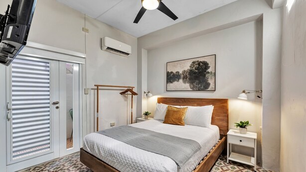 Ein Schlafzimmer mit Bett, Deckenventilator, Klimaanlage, einem Gemälde und Fliesenboden.