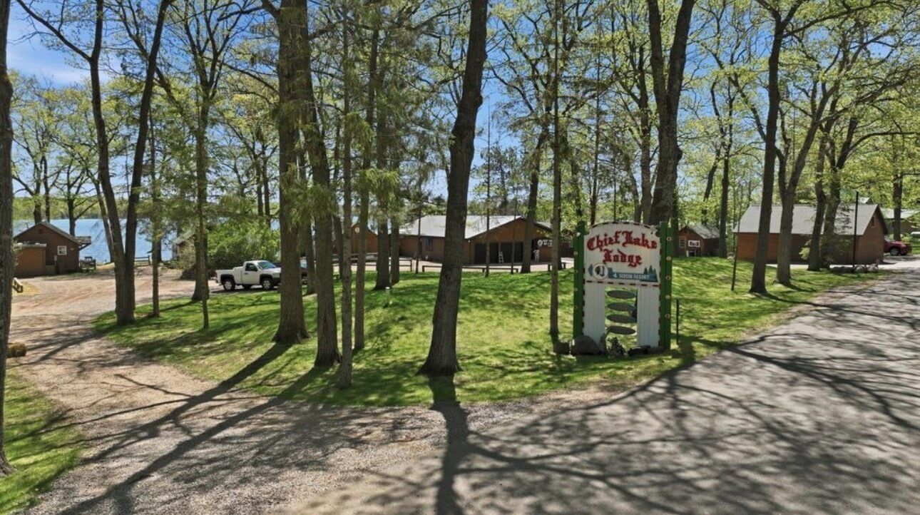 A campground with a sign for 'Chalet du Lac' and a lake in the background.