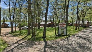 Um camping com uma placa para 'Chalet du Lac' e um lago ao fundo.