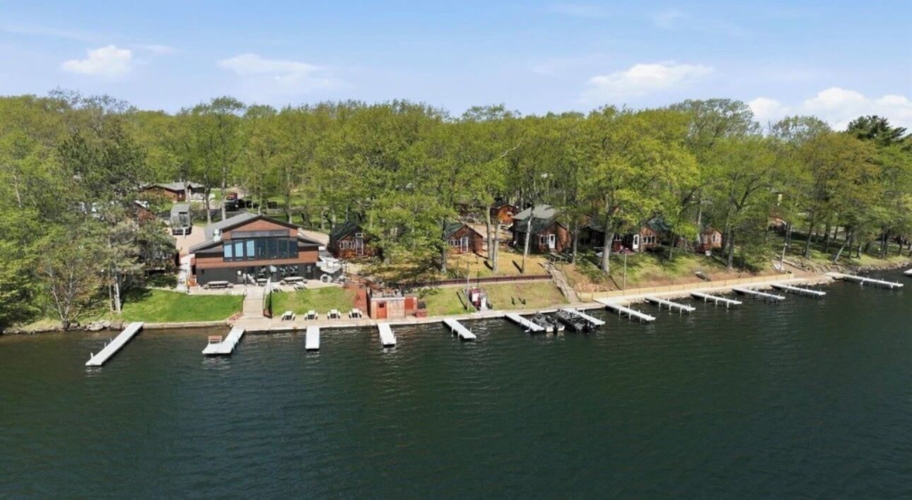 A lakeside property with docked boats, a large building with a glass facade, and surrounding trees.