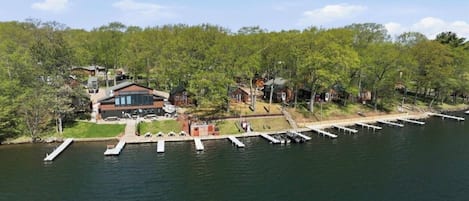 A lakeside property with docked boats, a large building with a glass facade, and surrounding trees.
