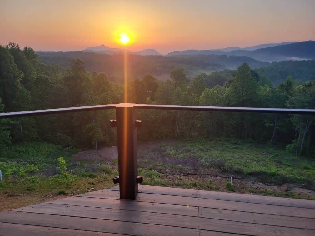 Una terraza de madera con barandilla metálica que da vista a un paisaje boscoso al atardecer.