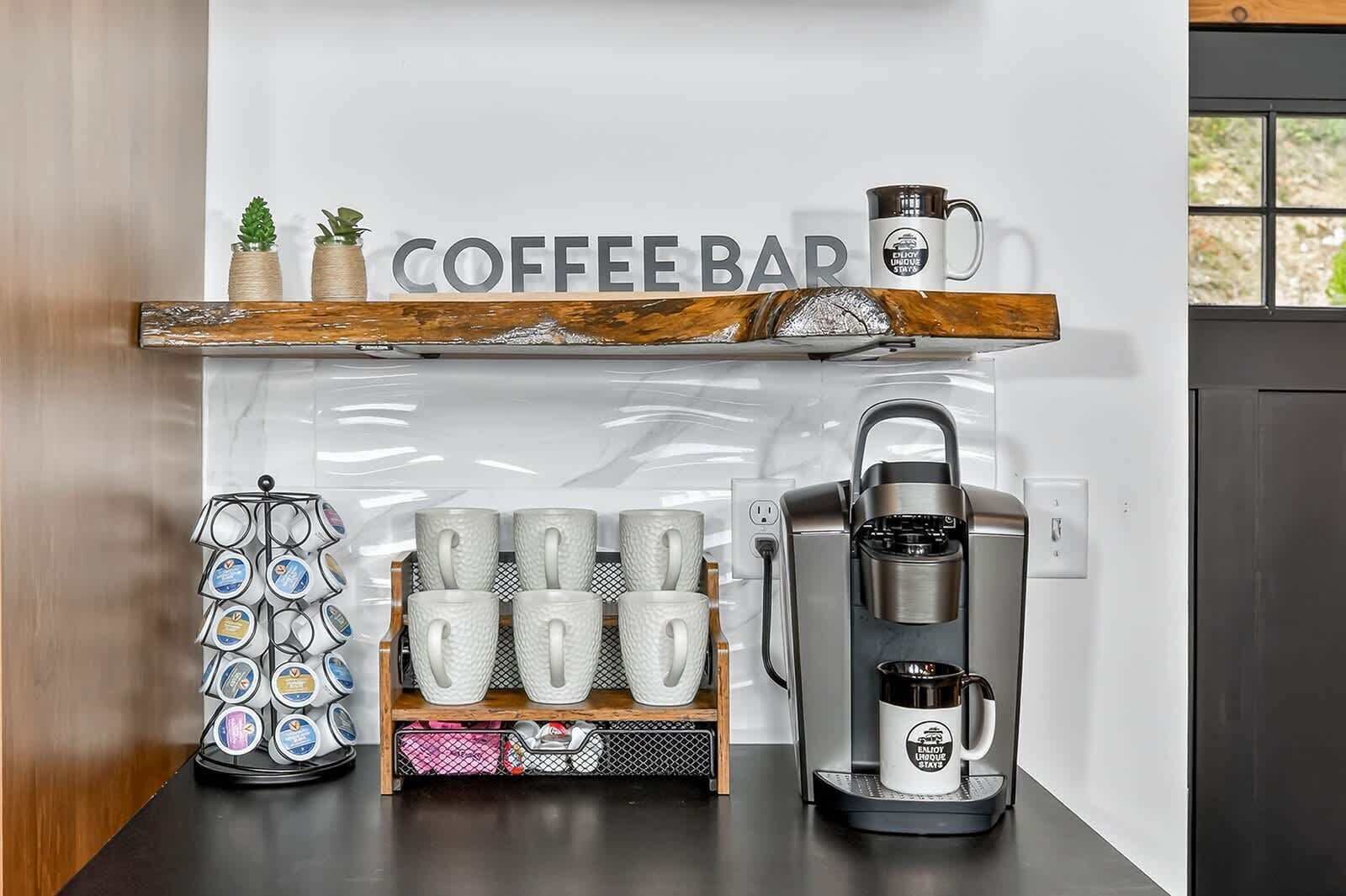 A coffee bar area with a coffee machine, a mug rack, and a coffee press on a counter.