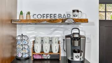 A coffee bar area with a coffee machine, a mug rack, and a coffee press on a counter.