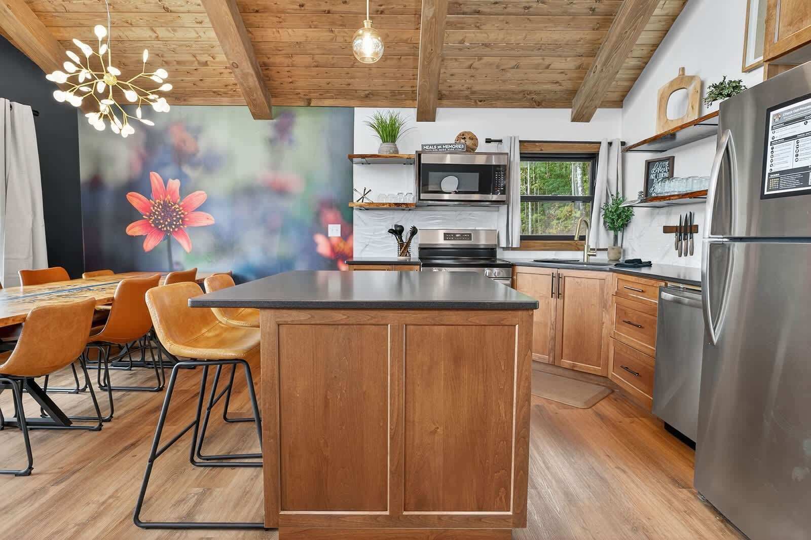 Eine moderne Küche mit Holzschränken, einer zentralen Kochinsel, Edelstahlgeräten und einem Essbereich mit Stühlen und einem Tisch.