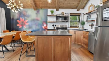 Eine moderne Küche mit Holzschränken, einer zentralen Kochinsel, Edelstahlgeräten und einem Essbereich mit Stühlen und einem Tisch.