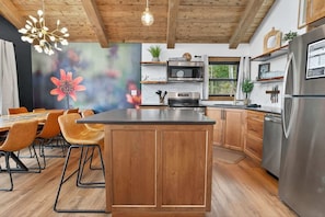Een moderne keuken met houten kastjes, een centraal eiland, roestvrijstalen apparatuur en een eethoek met stoelen en een tafel.