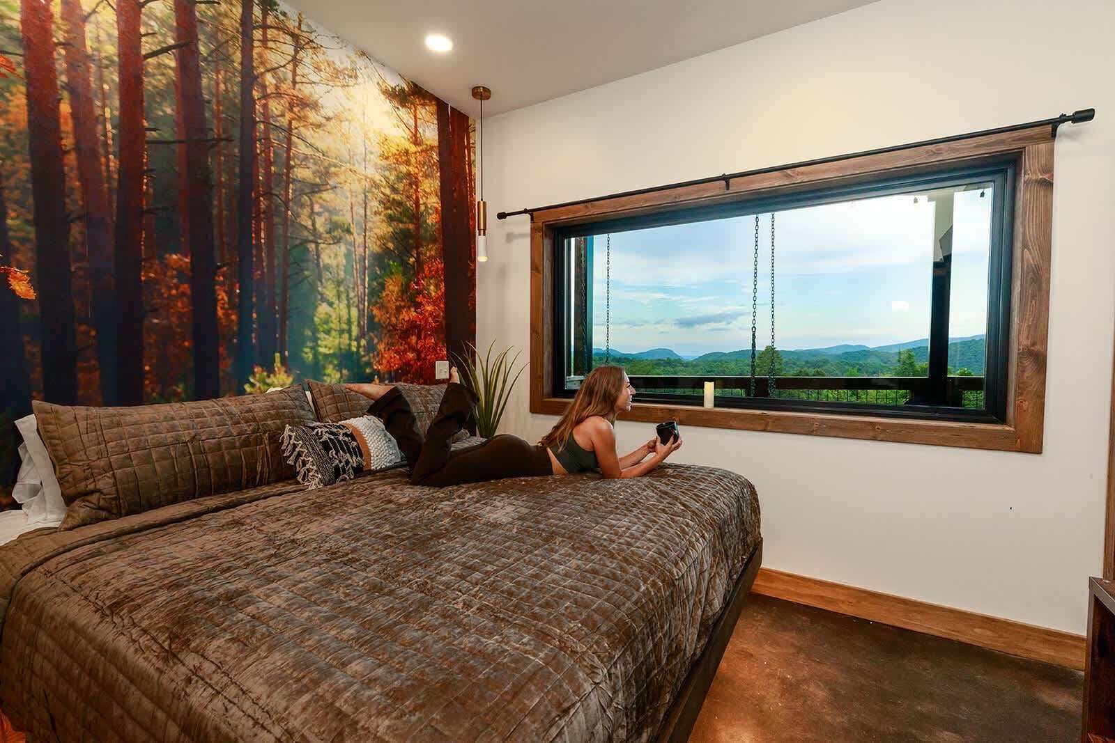 Quarto com uma cama grande, vista para o exterior pela janela e um mural na parede.