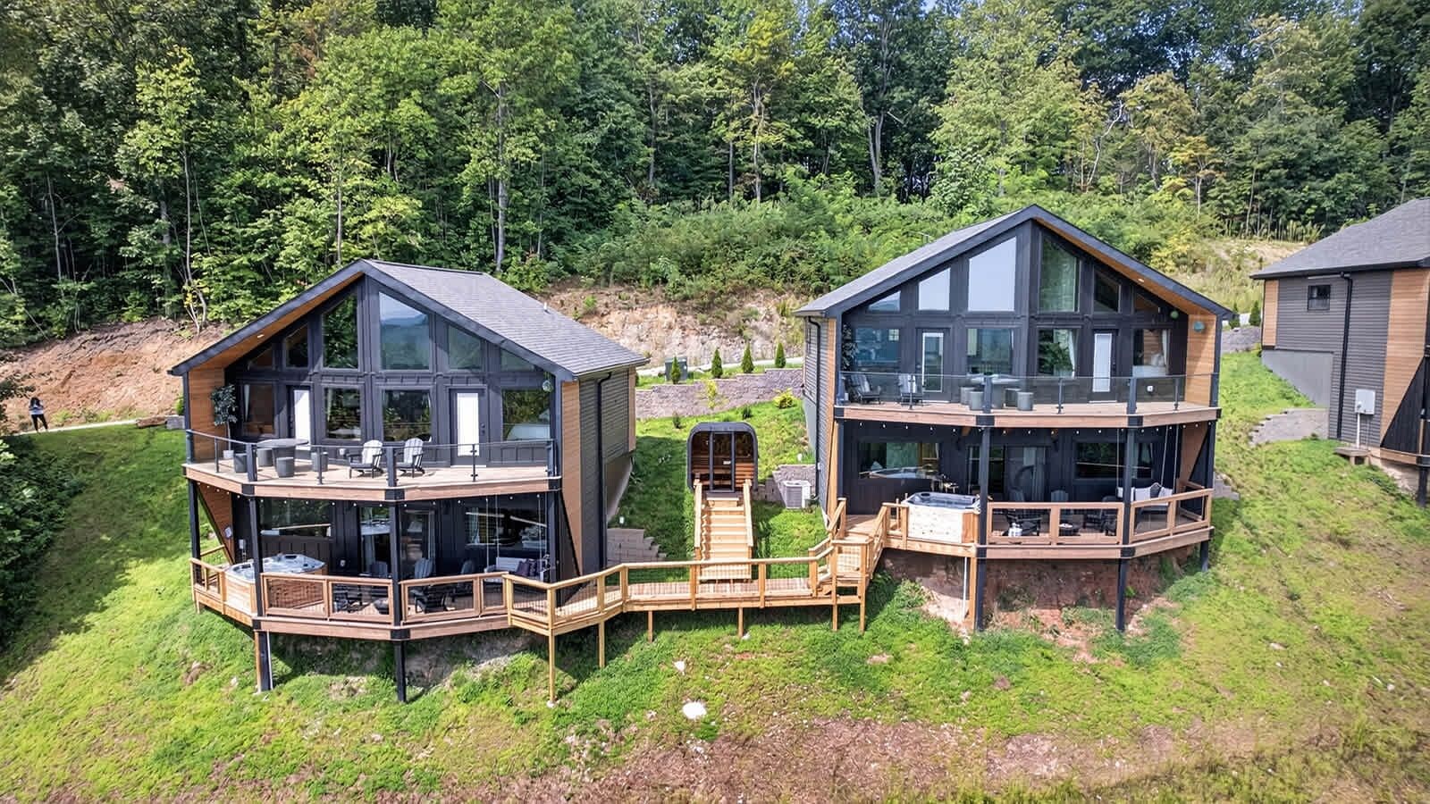 Zwei moderne Ferienhäuser mit Glasfassaden, Holzterrassen und Sitzbereichen im Freien.