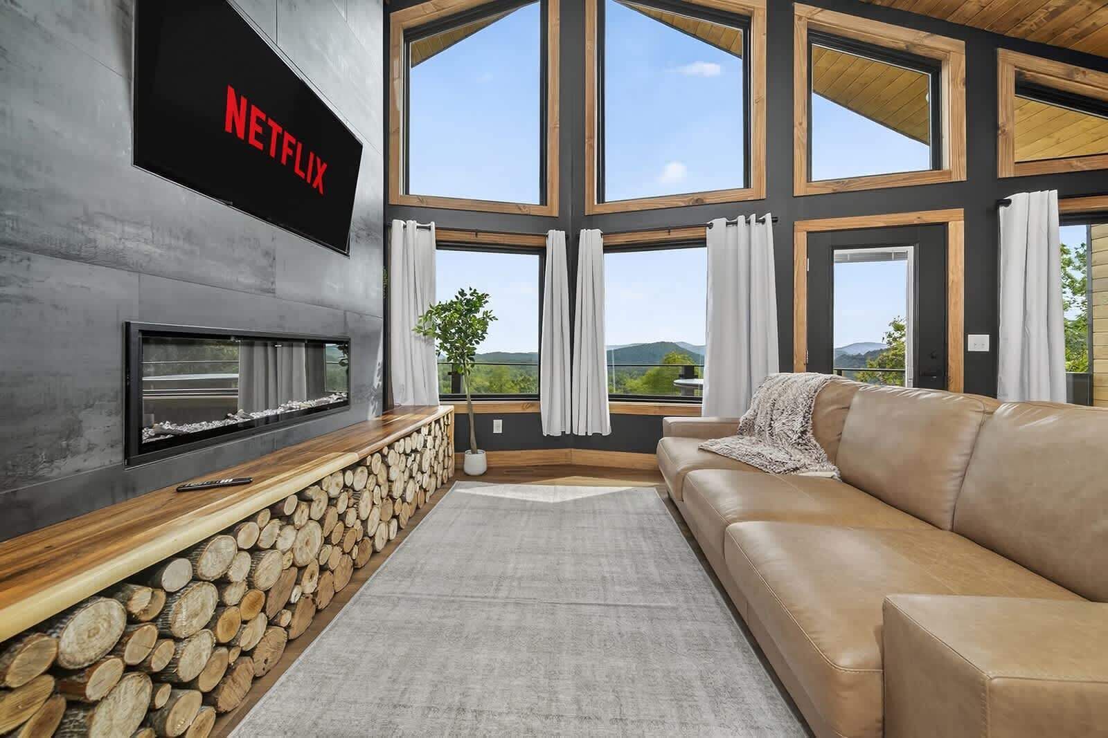 Una sala de estar moderna con un letrero de Netflix, una chimenea, un sofá y ventanas amplias.