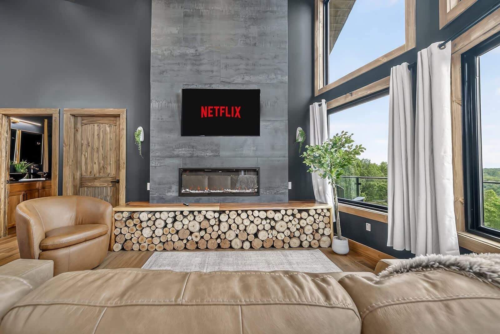 A modern living room with a fireplace, a mounted television displaying 'NETFLIX,' and a large window with curtains.