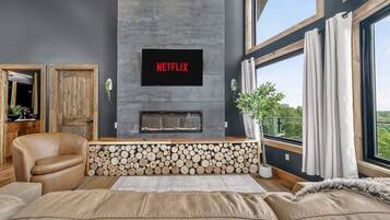 A modern living room with a fireplace, a mounted television displaying 'NETFLIX,' and a large window with curtains.