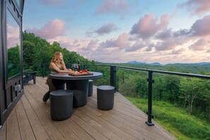 Eine Person sitzt an einem runden Tisch mit Blick auf eine bewaldete Landschaft.
