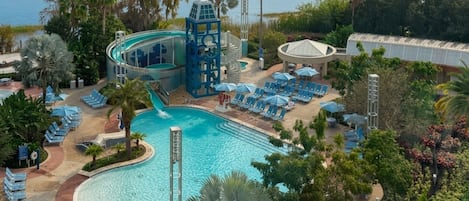Área de piscina em resort com escorregador, cadeiras de praia e palmeiras.