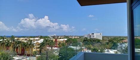 A balcony with a clear view of a cityscape, including buildings and a distant coastline.