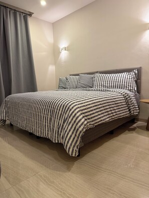 A bedroom with a bed, grey curtains, a wall-mounted light, and a tiled floor. - Galia Cozumel  (Cozumel)