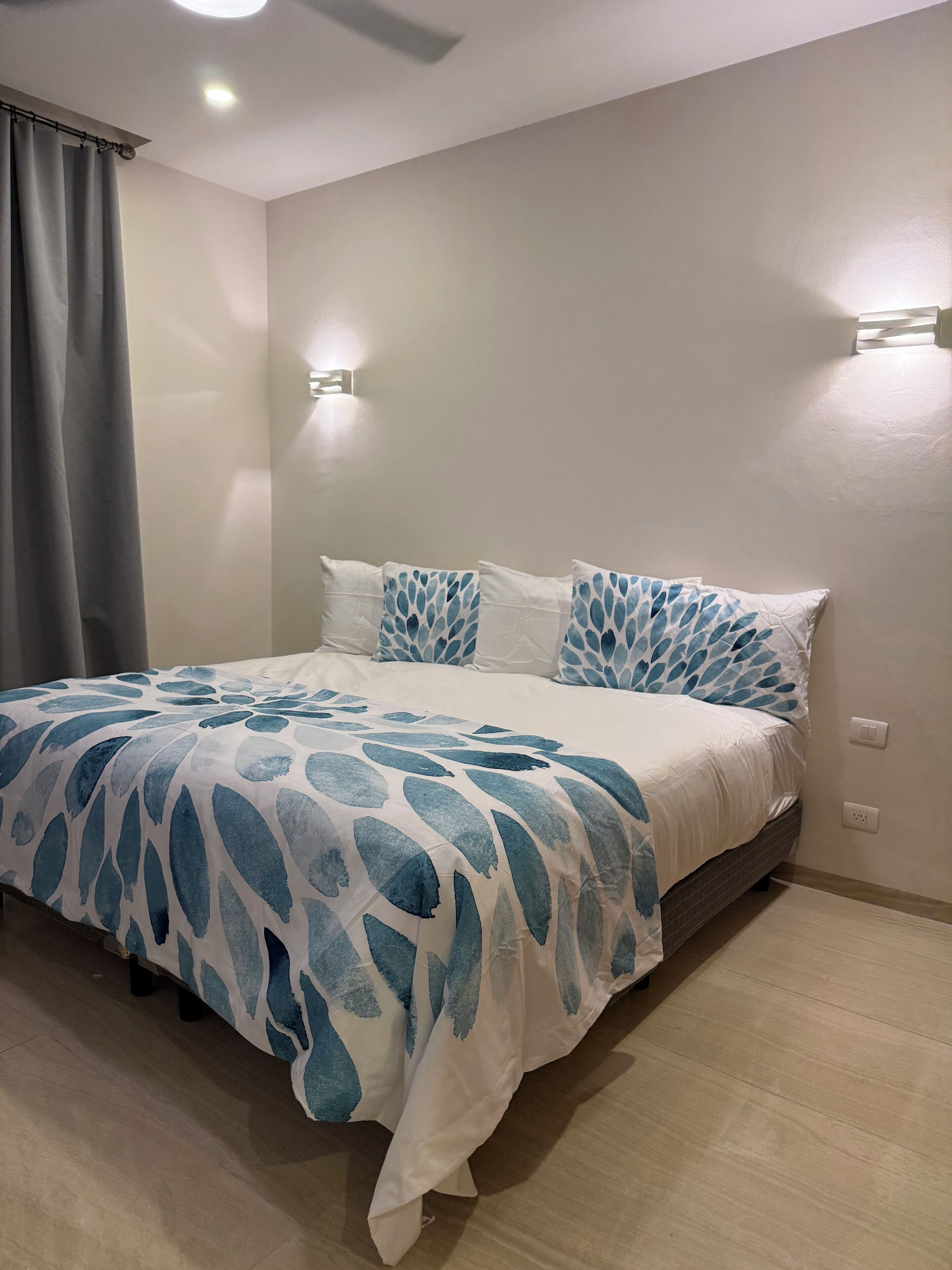 A bedroom with a bed, grey curtains, and wall-mounted lights.