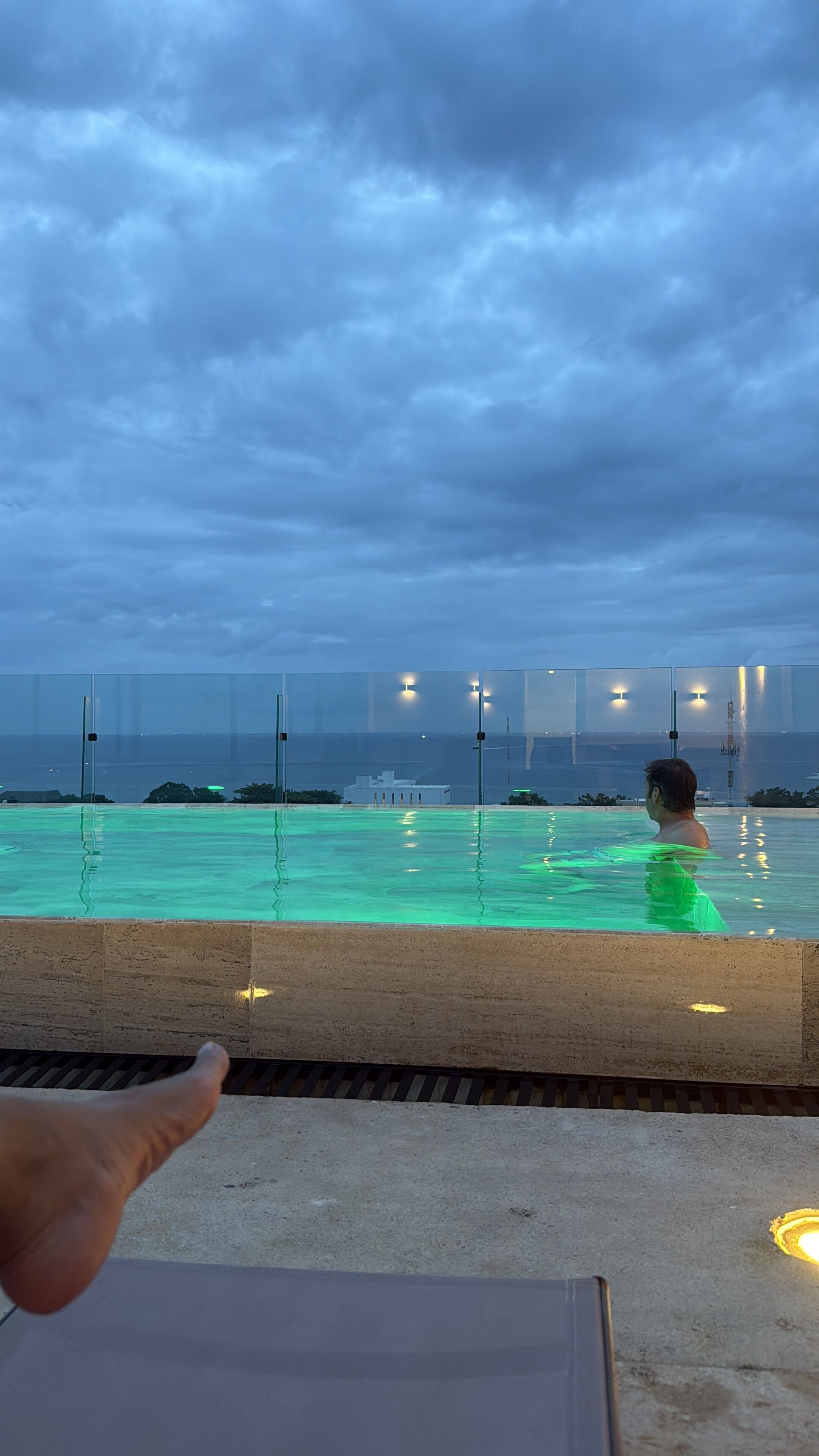 A swimming pool with a person in the water, a view of the sea, and a cloudy sky.