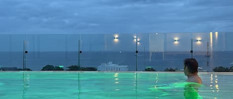 A swimming pool with a person in the water, a view of the sea, and a cloudy sky.