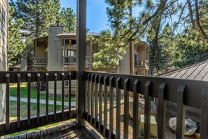 A wooden balcony with a view of a building complex, including a multi-story structure with balconies and a paved area with trees. - Spacious 2BR + Loft Mammoth Escape 680 (Mammoth Lakes)