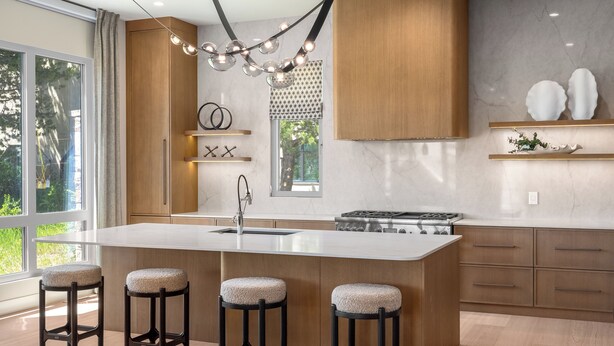 Une cuisine moderne dotée d’un îlot central, de tabourets de bar, de meubles en bois et d’un luminaire suspendu.