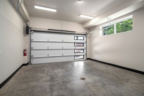 Eine Garage mit einer großen Rolltür, einem Feuerlöscher und einem Fenster mit Blick auf Grünflächen.