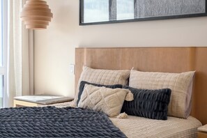 Ein Schlafzimmer mit einem Holzkopfteil, einem Bett mit vielen Kissen, einer dunklen Decke und einem Nachttisch.