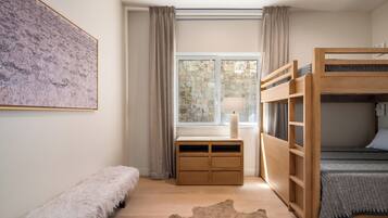 A bedroom with a bunk bed, a desk with a lamp, a fluffy bench, and a stone wall.