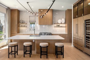 A modern kitchen with a central island, bar stools, wooden cabinets, and a built-in oven. - Close to Gondola Townhome 1097 (Steamboat Springs)