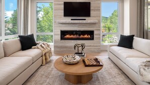 Un salon moderne avec une cheminée, un téléviseur à écran plat et un jeu d’échecs posé sur une table basse.